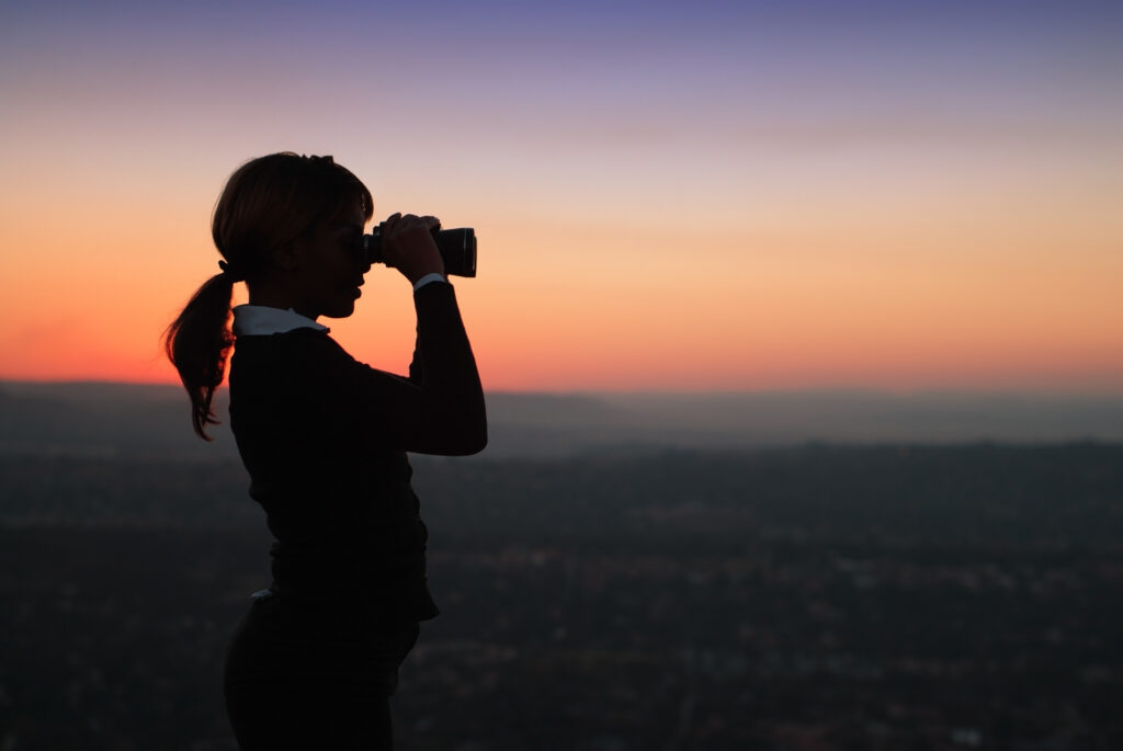 Looking through Binoculars Standing on a Hilltop