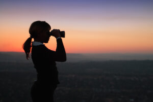 Looking through Binoculars Standing on a Hilltop